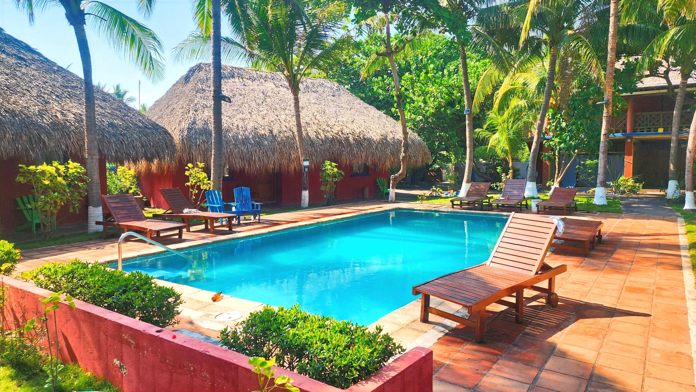 Piscina del hotel rodeada de vegetación y construcciones de techo de palma