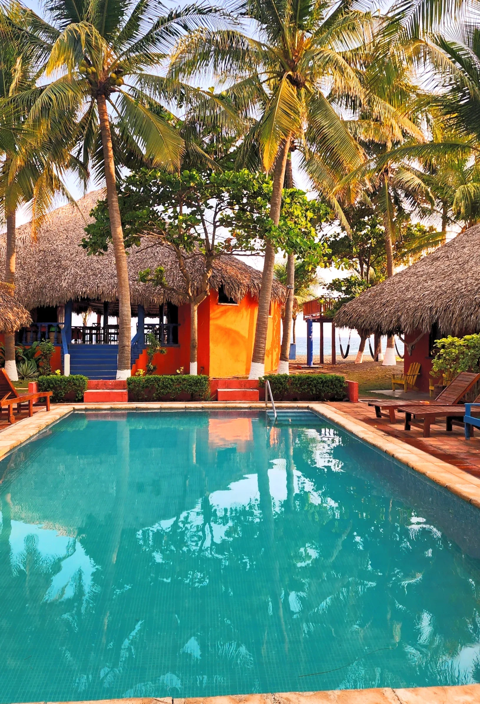 Exterior del hotel, con piscina, palmeras y edificios de colores